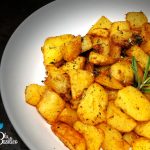 Cubetti di patate dorate in padella con rosmarino tritato e un rametto intero appoggiato sopra