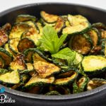 Rondelle di zucchine fritte condite con aceto, aglio e foglie di menta fresca in un piatto da portata