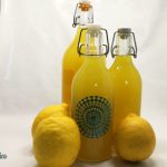 Bottiglie di limoncello fatto in casa dal colore giallo intenso accanto a limoni interi e scorze