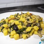 Piatto di gnocchi di patate con lupini sgusciati, cicoria verde e pomodorini in una padella con fondo di cottura
