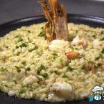 Piatto di risotto cremoso con asparagi verdi e gamberoni, guarnito con un filo di olio e asparagi crudi tritati