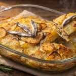 Pirofila di alici e patate al forno appena sfornata, con la superficie di patate dorata e gratinata
